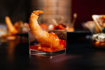 One fragrant large grilled king shrimp in red hot sauce in a glass.