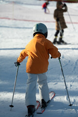 Child enjoying a sunny day skiing on a snowy slope with fellow skiers in the background...
