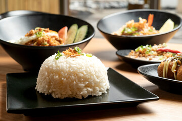 Close-up of a plate of steamed rice garnished with fried onions and spring onions, part of a selection of asian dishes