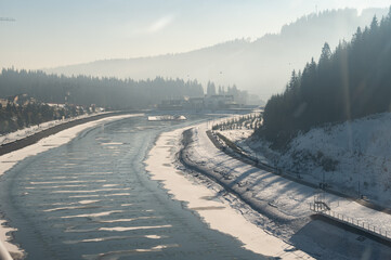 Majestic winter landscape of a frozen river snaking through pine forests and distant hills under a clear blue sky