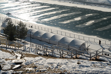 Winter landscape featuring a frozen river, snow-covered ground, and peaceful solitude near a quaint...