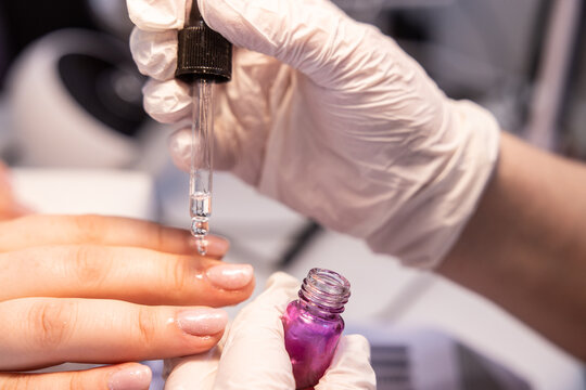 Nail technician applying cuticle oil during a manicure session