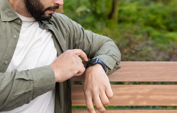 Man using a smartwatch while seated on a wooden bench in the city