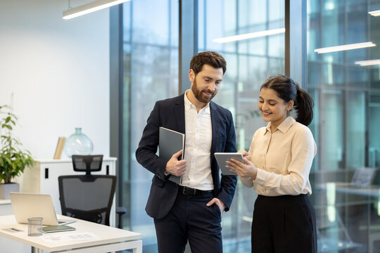 A businessman and businesswoman collaborate using a tablet in a bright, modern office setting.
