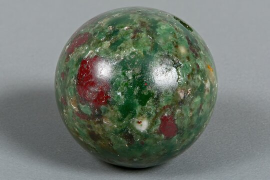 Polished sphere crafted from vibrant green and red mottled ruby in zoisite