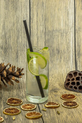 Refreshing lime cocktail with ice and dried citrus on rustic wooden background

