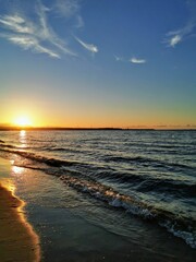 Serene sunset over the Baltic Sea in Gdańsk, Poland, with golden light reflecting on the waves and sandy beach under a blue sky.