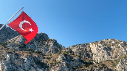 Off the coast of Datça, Turkey from the stern of a tour boat. It features the Turkish flag waving prominently against a backdrop of rugged cliffs and clear blue skies