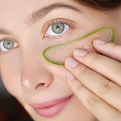 Beauty portrait of a  young woman with fair skin and green eyes applying a fresh aloe vera slice under her eye. Natural patches
