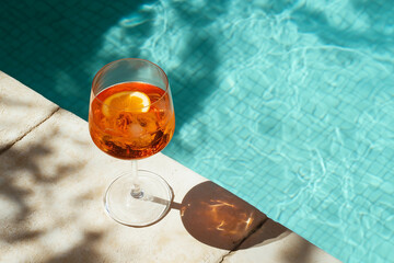 Cocktail aperol spritz on the tiles edge of the pool, shadows overlay	