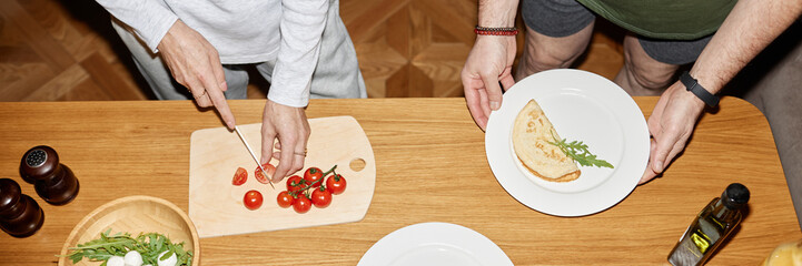 Website header shot of hands cutting tomatoes on cutting board next to plate with folded omelet and arugula while other person holding bowl with greens