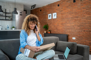 Woman opening parcel at home and talking on mobile phone