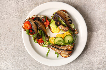 Plate of tasty sandwiches with canned smoked sprats on grey background