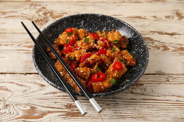Bowl with tasty sweet and sour chicken on light wooden background, closeup