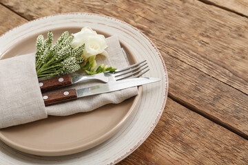 Beautiful table setting with cutlery and floral decor folded in napkin on wooden table