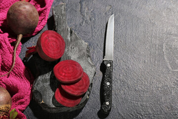 Wooden cutting board with beet and knife on black background