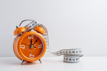 Alarm clock with measuring tapes, copy space. Healthy lifestyle, weight loss 
