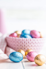Chocolate easter eggs wrapped in multi colored foil on white table.