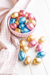 Chocolate easter eggs wrapped in multi colored foil in bowl on white table.