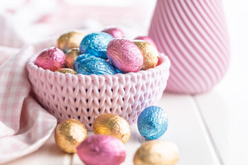 Chocolate easter eggs wrapped in multi colored foil in bowl on white table.