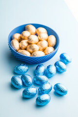 Chocolate easter eggs wrapped in blue colored foil on blue background.