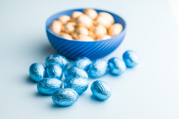 Chocolate easter eggs wrapped in blue colored foil on blue background.