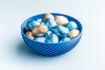 Chocolate easter eggs wrapped in multi colored foil on blue background.