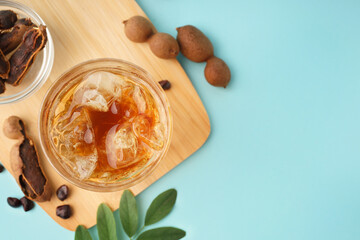 Glass of tasty tamarind drink and fruits on blue background