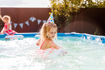 Blonde curly-haired 6-7-year-old girl swimming in a backyard pool during summer, celebrating her...