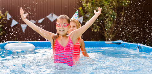 Red haired 7-8 year old girl celebrating her birthday in a summer pool, jumping in the water and splashing