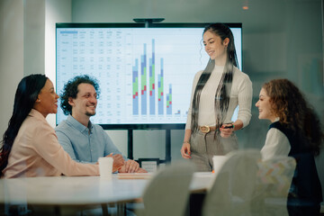 Businesswoman leading presentation, showing charts on monitor to colleagues in meeting room