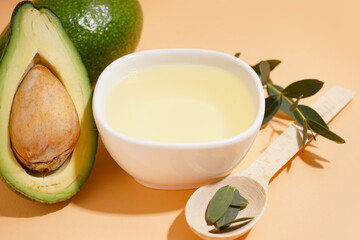 Fresh avocados with wooden spoon and bowl of essential oil on beige background