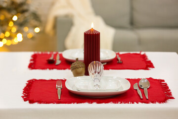 Beautiful table setting with candle and red napkins for Christmas dinner in living room