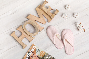Soft slippers with word HOME and cotton flowers on floor