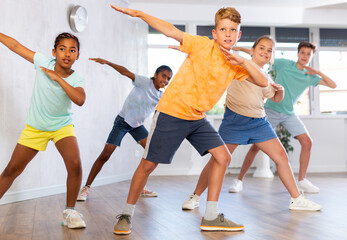 Male child perform choreographic exercises and teaches energetic mobile social dance hip hop together with friends. Young girls and guys repeat movements, train in spacious studio unfocused