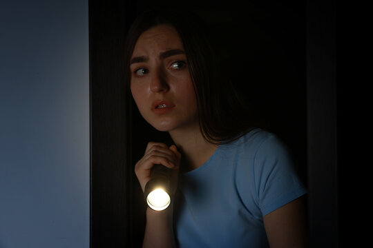 Fear of darkness. Scared young woman with flashlight indoors at night