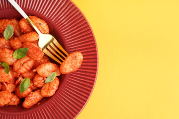 Plate of tasty gnocchi with tomato sauce on yellow background