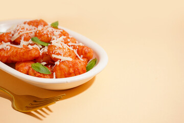 Plate of tasty gnocchi with tomato sauce and cheese on beige background