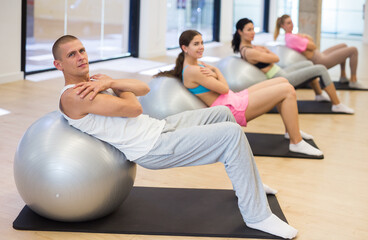 Group of adult sports people engaged in fitness in the studio perform a back stretching exercise...