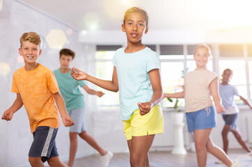 Dynamic little girl training Rock-and-Roll dance poses in dancehall with other attendees of dancing...