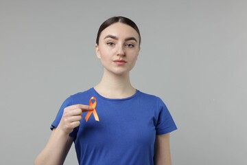 Multiple Sclerosis awareness. Young woman holding orange ribbon on light grey background