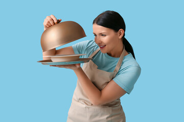 Beautiful young waitress with tray and cloche on blue background