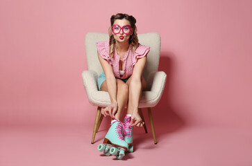Attractive pin-up woman in roller skates sitting on armchair against pink background