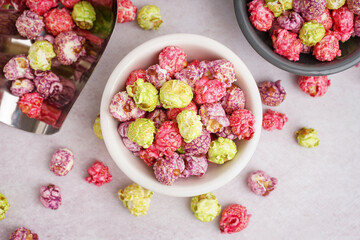 Bowls and metal scoop with sweet colorful popcorn on white background