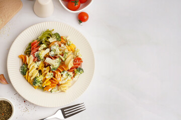 Delicious fusilli pasta with broccoli in plate and tomatoes on light background