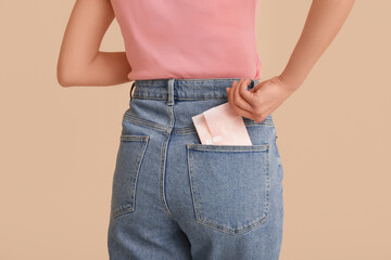 Woman putting menstrual pad into pocket on beige background