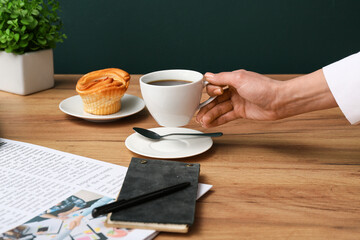 Female hand holding cup of coffee with newspapers and notebook on wooden table