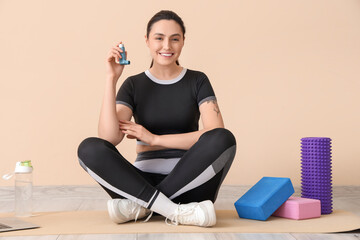 Young woman with inhaler and sports equipment sitting near beige wall