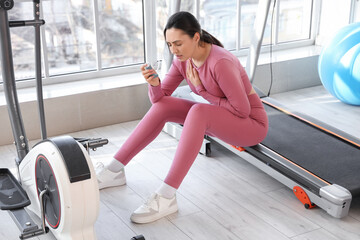 Sporty young woman with inhaler having asthma attack in gym