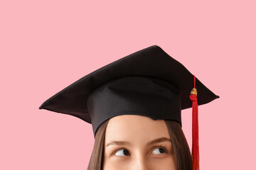 Young female graduate with graduation hat on pink background, closeup